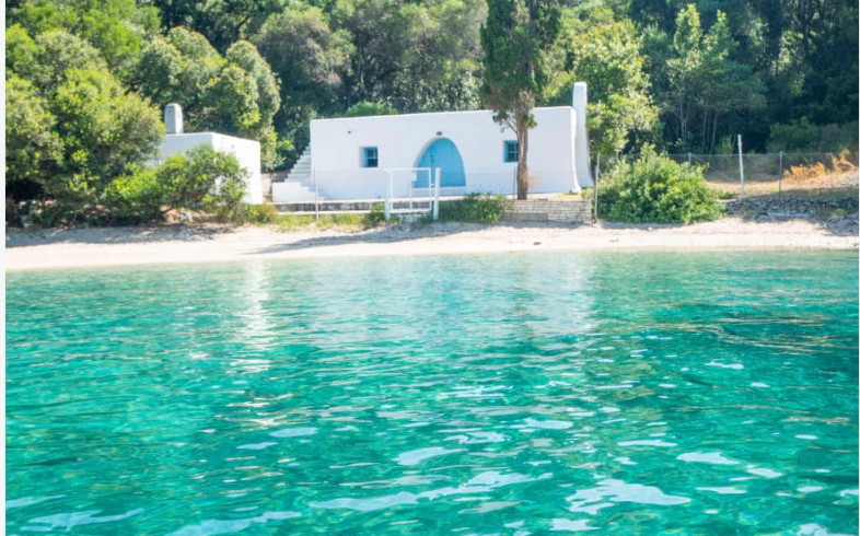 White cottage on Skorpios island beach with turquoise water near Lefkada